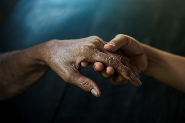 Young woman holding older nursing home patient's hand.